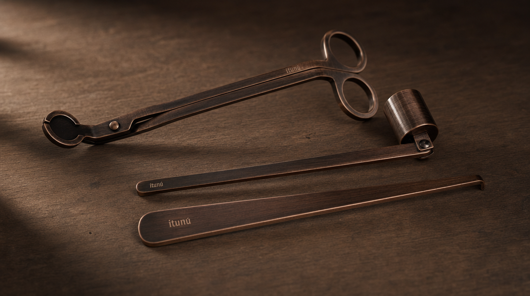 The three Ọ̀nà tools in antique bronze on a dark walnut bench: the scissor wick trimmer with its dogleg arm and round cutting disc, the snuffer with its cylindrical cup on a hinge, and the tapered wick aligner with its hooked tip. Each is etched ìtùnú.